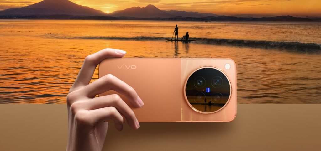 فيفو توسع طرح سلسلة vivo X500 عالمياً مع كاميرات ZEISS وبطاريات كبيرة هاتف من سلسلة vivo X500 باللون البرتقالي أمام مشهد بحر وقت الغروب